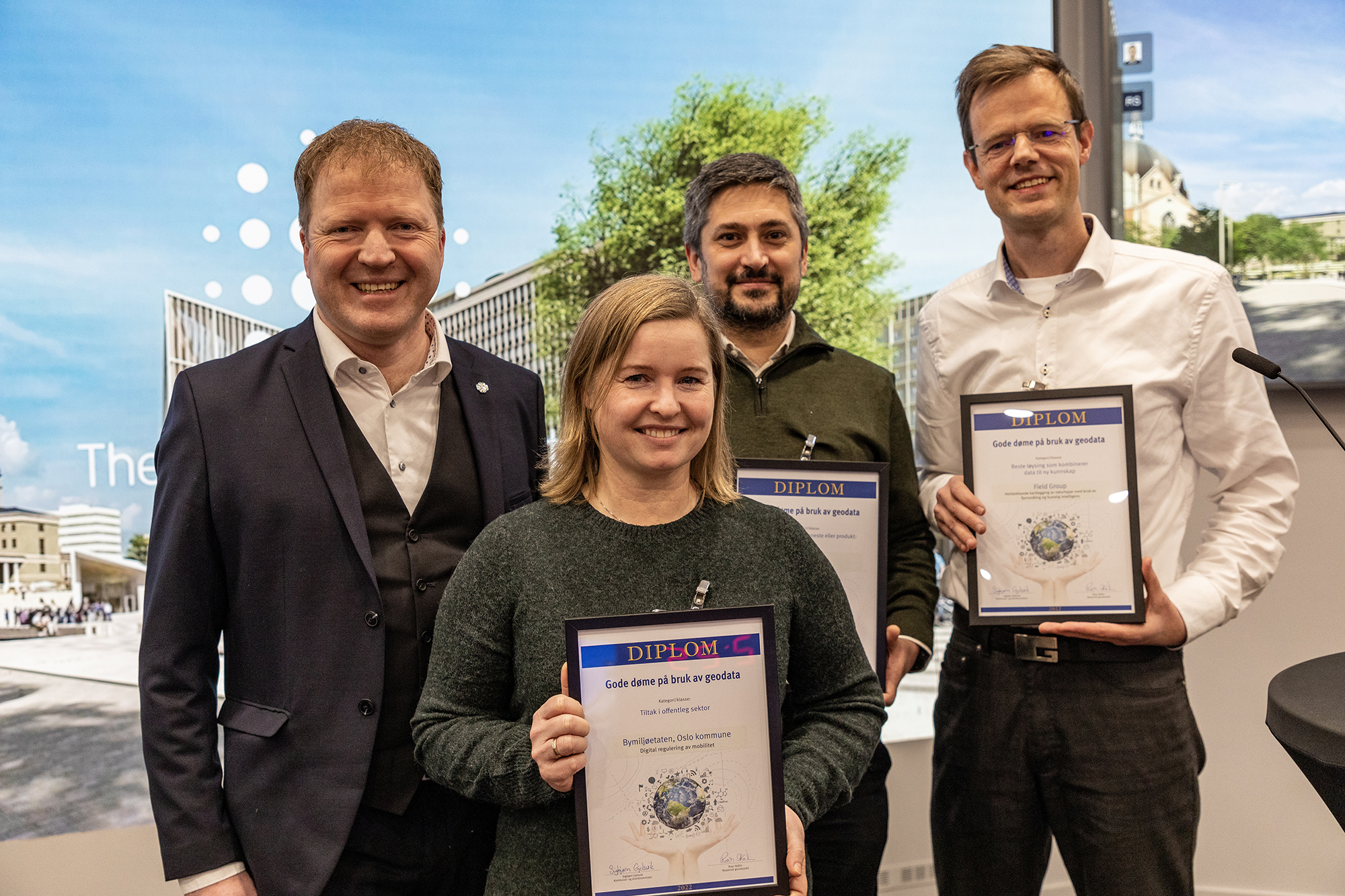 Statsråd Sigbjørn Gjelsvik og dei tre premievinnarane i 2022, ei dame og to menn. Alle vinnarane held eit innramma diplom.