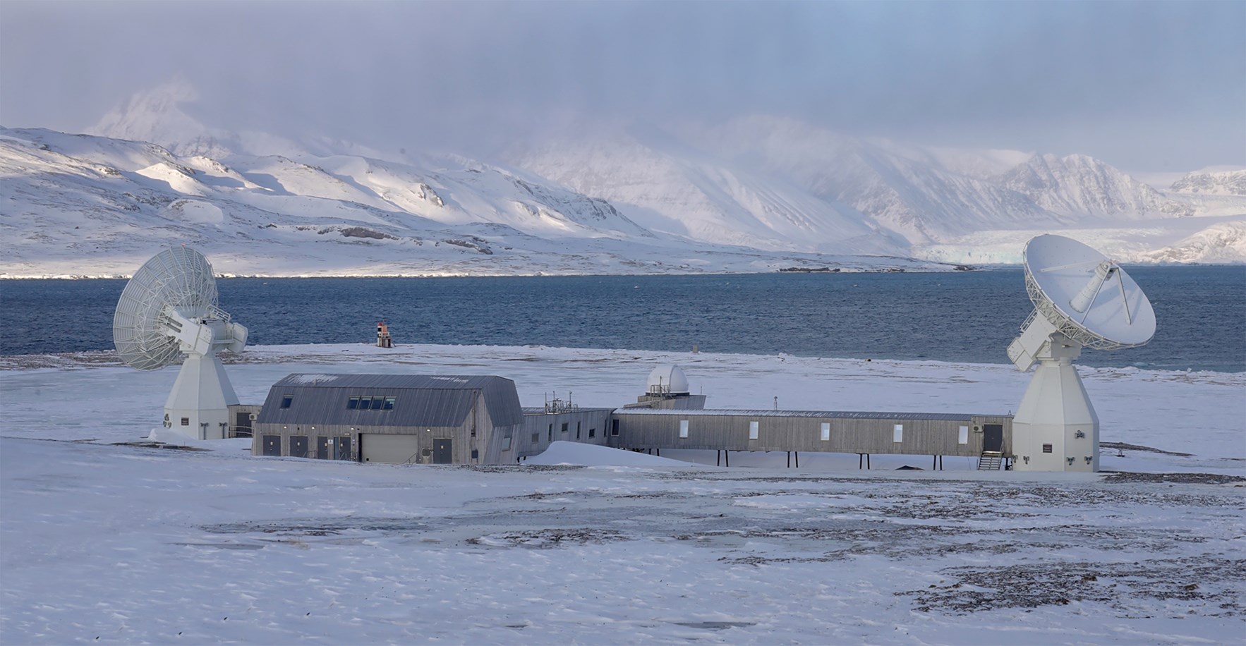 Jordobservatoriet i Ny-&Aring;lesund p&aring; Svalbard med med satelittmottakere og arktisk landskap i bakgrunnen.