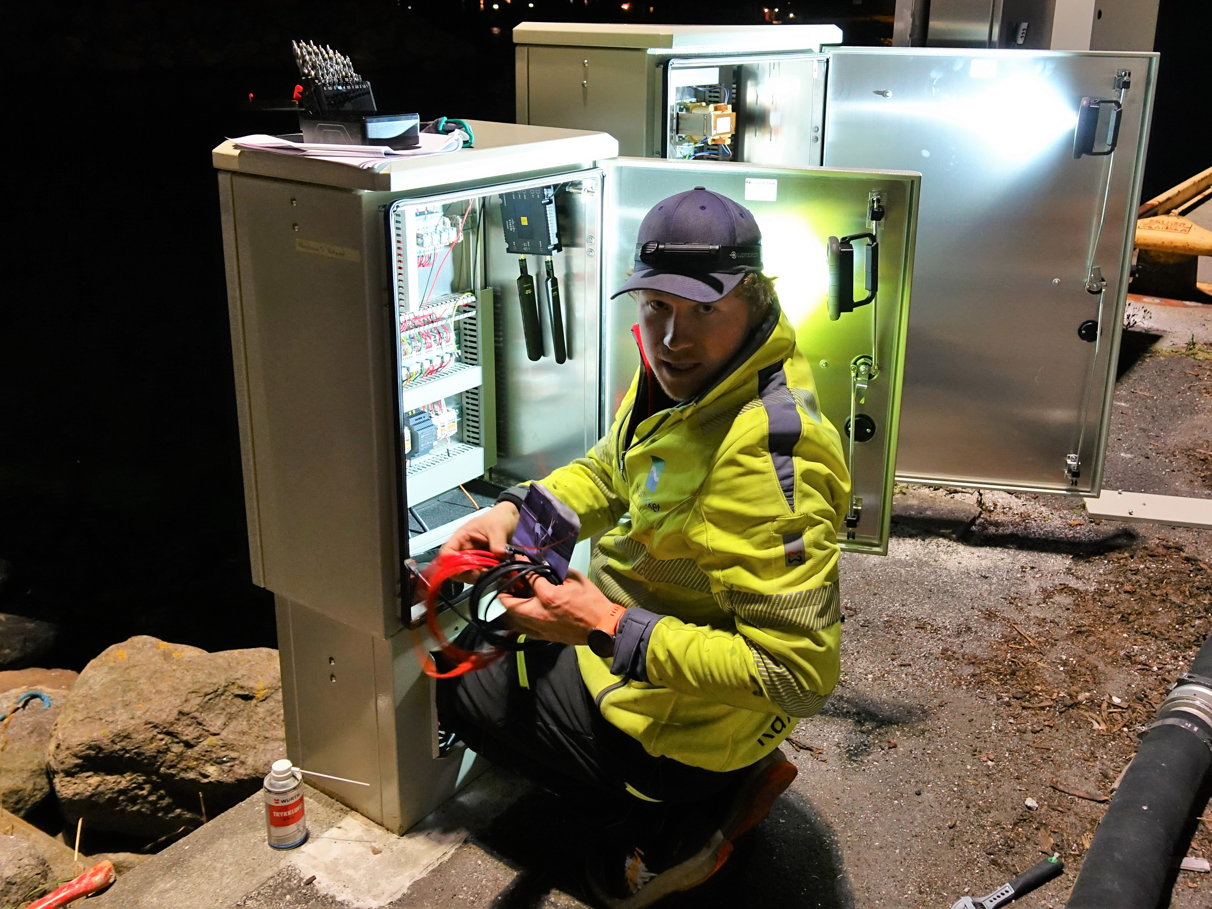 Mann monterer koblinger til vannstandm&aring;ler inni et sikringsskap p&aring; ei kai i Sirev&aring;g p&aring; J&aelig;ren. Foto.