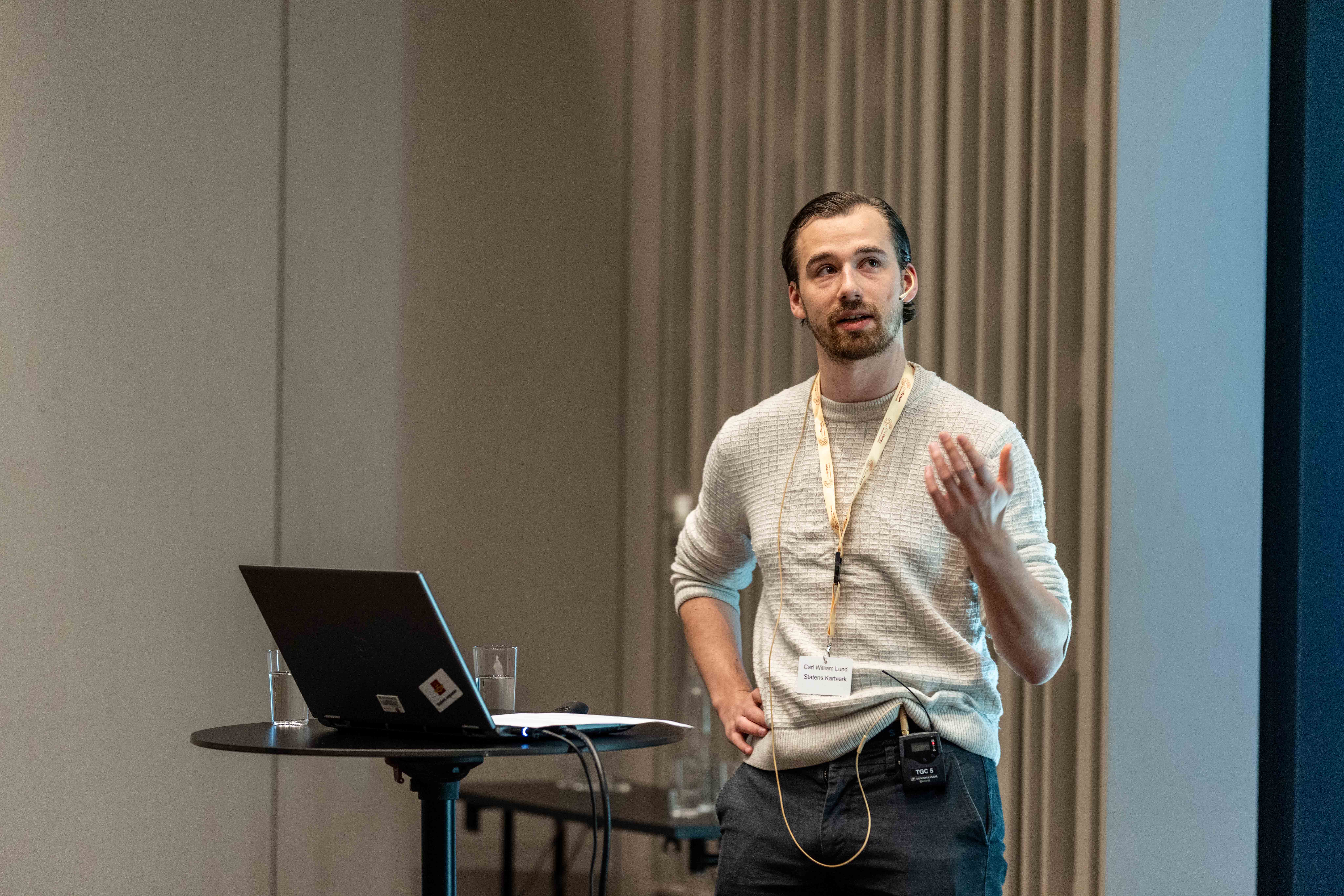 Mannlig kartverksansatt Carl William Lund viser taktile kart p&aring; Geomatikkdagene 2025